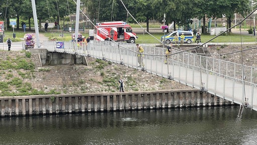 Auf einer Brücke und am Wasserrand stehen Einsatzkräfte und Fahrzeuge der Feuerwehr und Polizei