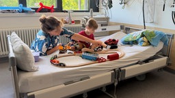 Krankes kind sitzt im Bett und spielt mit der Oma Autorennen