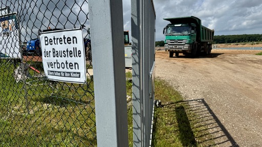Bauzaun vor einem Bagger, der Kies am Niederrhein abbaut
