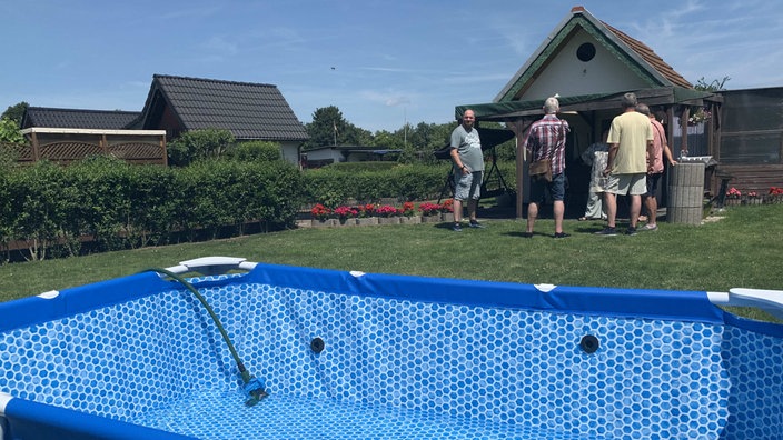 Der Vorstand des Kleingartenvereins "Feierabend" im Hintergrund schauen auf den Pool im Vordergrund