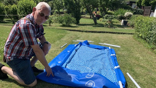 Jörg Wagner, Vorsitzender des Kleingartenvereins "Feierabend", kniet neben einem noch nicht aufgebautem Pool.