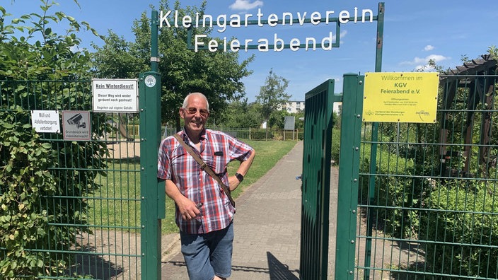 Jörg Wagner, ein Mann mit Sonnenbrille und kurzem Hemd, steht am offenen Eingangstor des Kleingartenvereins Feierabend