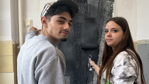 Zwei Schüler streichen eine Wand mit schwarzer Farbe