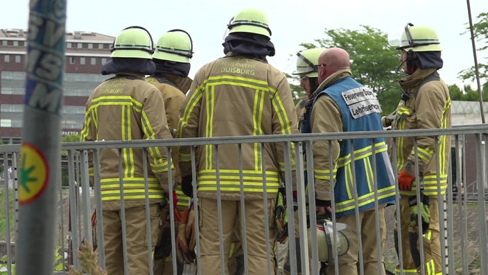 Mehrere Feuerwehrleute der Feuerwehr Duisburg in Schutzkleidung stehen mit dem Rücken zur Kamera nah beieinander