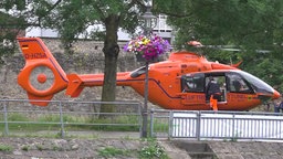 Ein oranger Hubschrauber der Luftrettung steht auf einer Wiese. Ein Mann in Einsatzkleidung steigt ein.