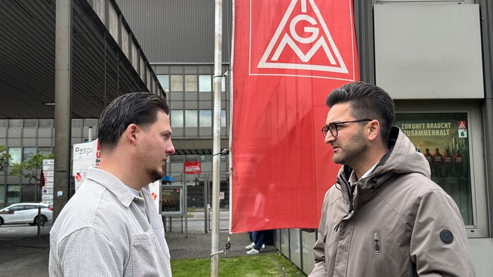 Zwei Männer stehen sich vor einem "IGM"-Banner gegenüber.