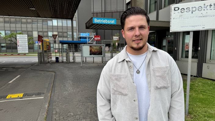 Raphael Taverna steht vor einem Thyssenkrupp-Gebäude und schaut in die Kamera. Neben ihm ist ein Schild mit der Aufschrift "Respekt".