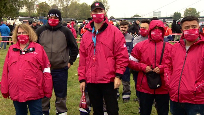 Menschen mit roter Maske und Regenkleidung demonstrieren in einer Gruppe.