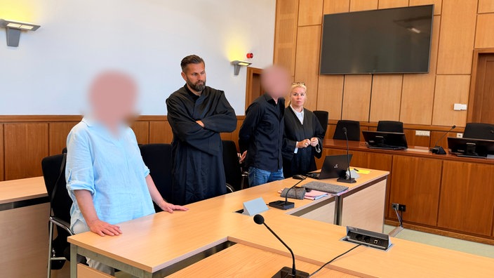 Die Angeklagten stehen neben Verteidiger und Verteidigerin im Gerichtssaal.