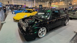 Ein schwarzer VW Golf und ein gelber Porsche sind in der Messe Essen ausgestellt