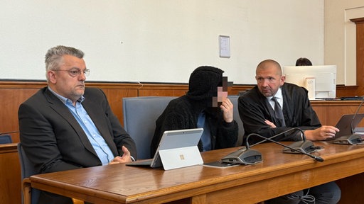 Angeklagter sitzt neben Verteidiger und Dolmetscher im Gerichtssaal