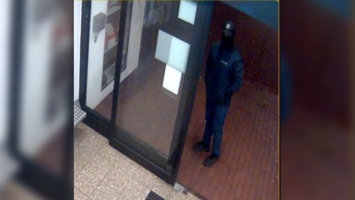 Ein dunkel gekleideter Mann mit Sturmhaube steht neben dem Kassenautomat eines Parkhauses