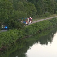Einsatzwagen der Feuerwehr und Polizei stehen auf dem Weg neben einem Fluss.