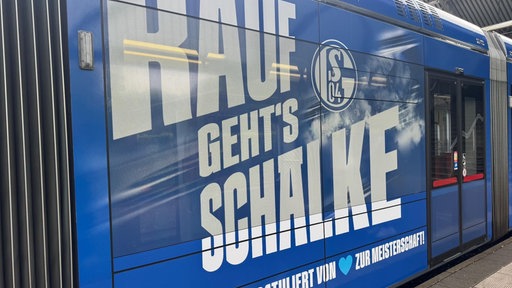 Rauf gehts Schalke steht in weißer Schrift auf einer blauen Straßenbahn