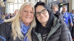 Zwei Frauen stehen nebeneinander, halten die Köpfe aneinander und lachen in die Kamera