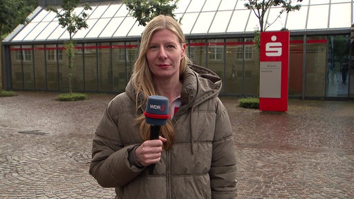 WDR-Reporterin Jennifer Kerkhoff hält ein Mikrofon in der Hand und lächelt in die Kamera.
