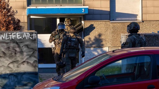 Vier Polizisten kommen aus einem Wohnhaus