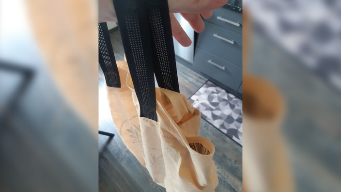 Beige Stofftasche mit schwarzen Henkeln, die in einer Hand gehalten wird und teilweise geöffnet ist.