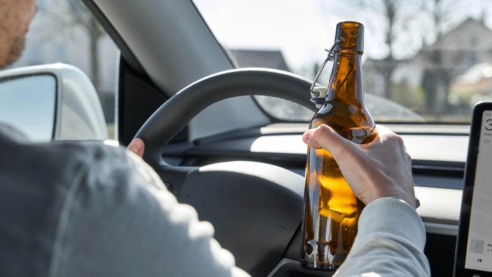 Ein Autofahrer hält während der Fahrt eine Flasche Bier in der Hand