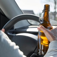Ein Autofahrer hält während der Fahrt eine Flasche Bier in der Hand