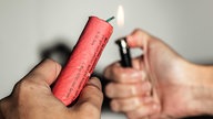 Eine Hand zündet mit einem Feuerzeug einen Böller in der anderen Hand an
