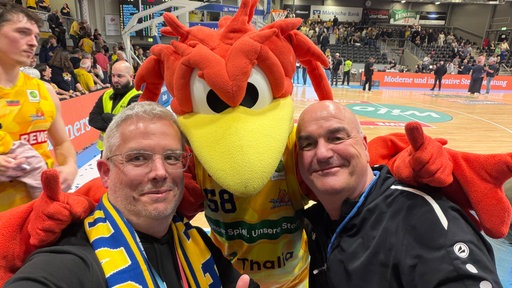 Selfie unseres Autors Christian Beisenherz mit dem Maskottchen Felix, einem roten Feuervogel, und WDR-Sportreporter Michael Bodenröder