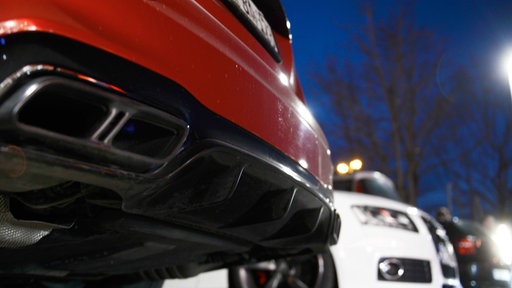 Auf dem Foto ist das Heck eines roten Sportwagens, daneben steht ein weißer Audi.