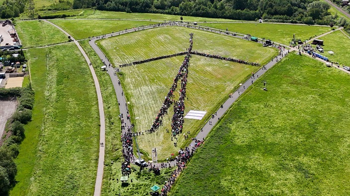Luftaufnahme: Menschen bilden gemeinsam die Form einer Windkraftanlage