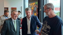 Drei Männen stehen nebeneinander und lachen gemeinsam.