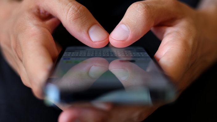 Auf dem Foto ist ein Smartphone, auf dem Finger etwas in einen Whatsapp-Chat tippen.