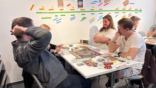 Vier Spieler sitzen an einem Tisch um ein Brettspiel herum