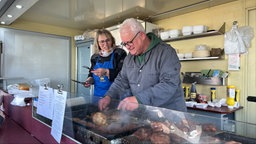 Zwei Personen stehen hinter der Theke eines Imbisswagens und braten Frikadellen