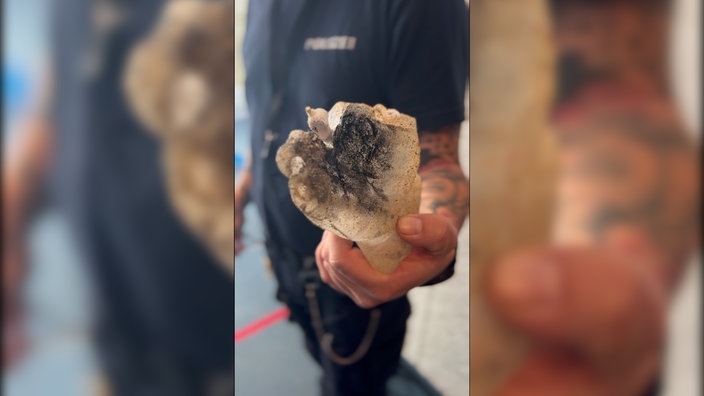 Ein männlicher Polizist hält die Überreste einer durch Böller zerfetzten Hand aus dem 3D-Drucker in seiner Hand