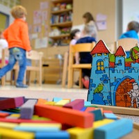 Eine Spielburg und Bauklötze, im Hintergrund unscharf mehrere Kinder in einer Kindergruppe