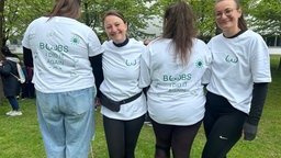 Zwei Frauen schauen in die Kamera und lächeln, zwei sind zur Kamera umgedreht mit dem Schriftzug auf dem T-Shirt: "Boobs I did it again"