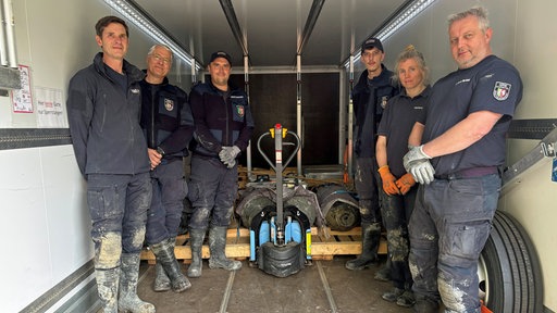 Mitarbeitende des Kampfmittelbeseitigungsdienstes stehen auf einer Ladefläche, auf der die entschärften Bomben liegen, und schauen in die Kamera.