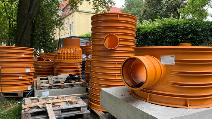 Orange große Rohre stehen auf Betonplatten vor dem Rathaus