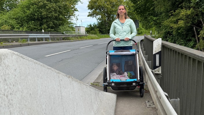 Eine Frau mit Kinderwagen steht vor einer Betongleitwand