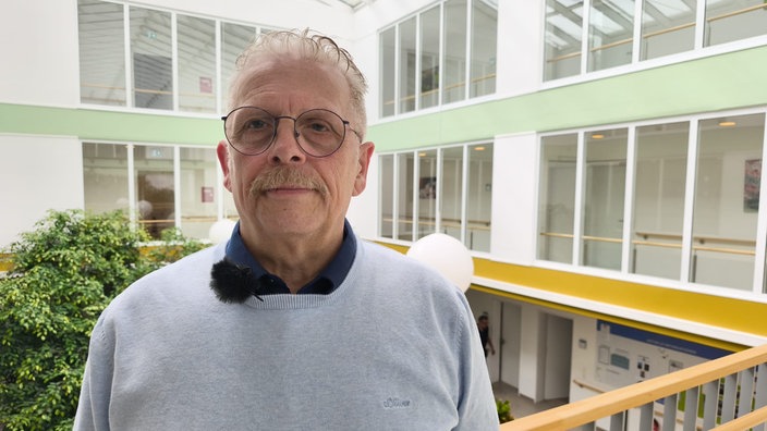 Dirk Schmadel steht in einem grauen Pullover in einem Pflegeheim