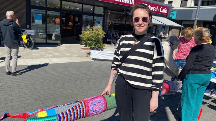 Jennifer Klemme steht neben dem umhäkelten Maibaum und schaut in die Kamera.