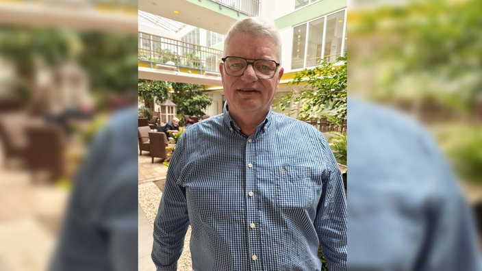 Michael Kamp steht in einem blau-weiß kariertem Hemd in einem Pflegeheim