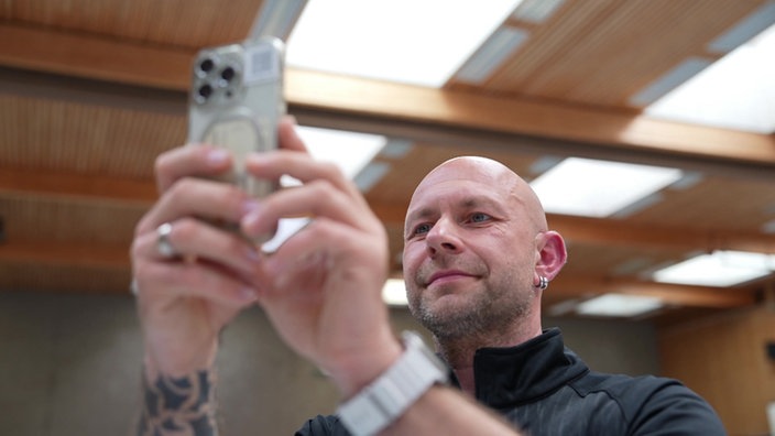 Ein Mann macht in einer Sporthalle Aufnahmen mit seinem Smartphone.