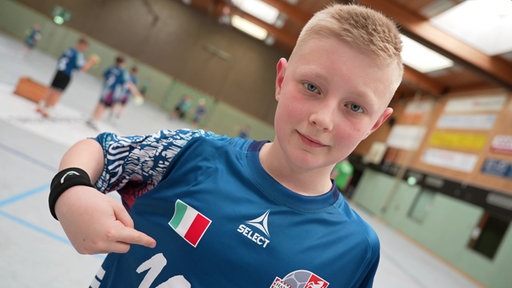 Ein Junge, Lennox Benna, steht im Italien-Handball-Trikot in einer Sporthalle.