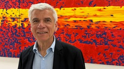 Ein Mann vor einem rot, gelben Bild von Gerhard Richter.