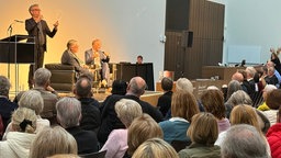 Man spricht auf einer Bühne vor einem Publikum