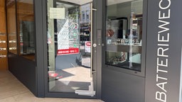 Die Tür zum Juwelier-Geschäft ist an einer unteren Ecke beschädigt und mit Klebeband beklebt. An der Tür hängt ein Zettel, der auf die Schließung des Ladens hinweist.