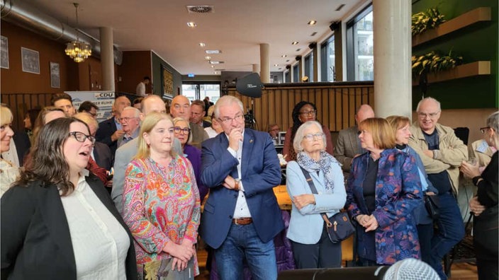 Eine Menschenmenge steht zusammen und schaut teils nachdenklich auf die Zwischenergebnisse der Stichwahl.