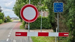 Ein Durchfahrt Verboten Schild mit einer Straßensperrung neben einem Verkerhrsschild auf dem "Niederlande" steht