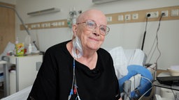 ältere Frau ohne Haar sitzt lächelnd im Krankenbett
