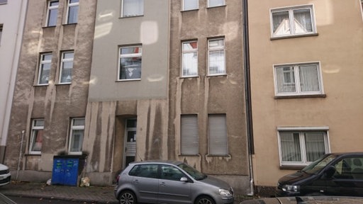Ein graues Mehrfamilienhaus mit geparkten Autos vor der Tür